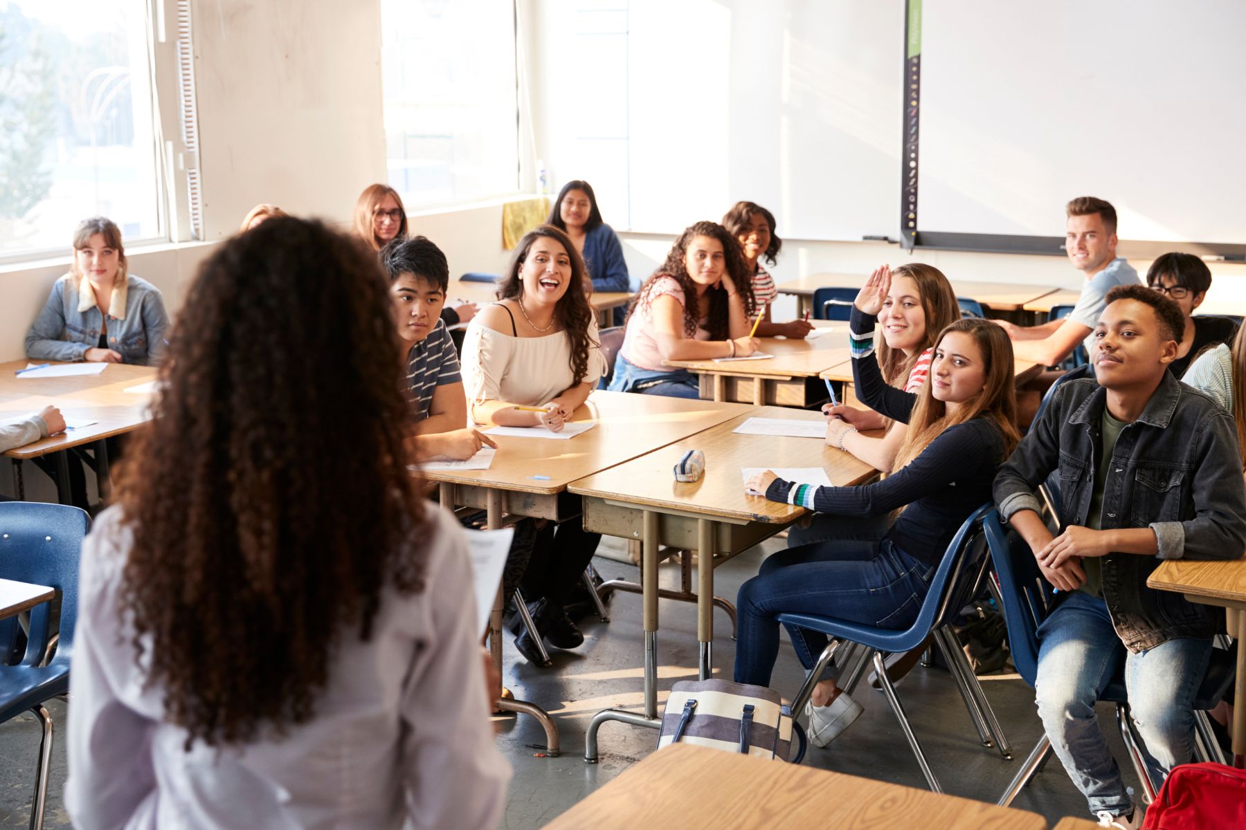 Klaslokaal met scholieren die aan tafel zitten-meisje steekt hand op