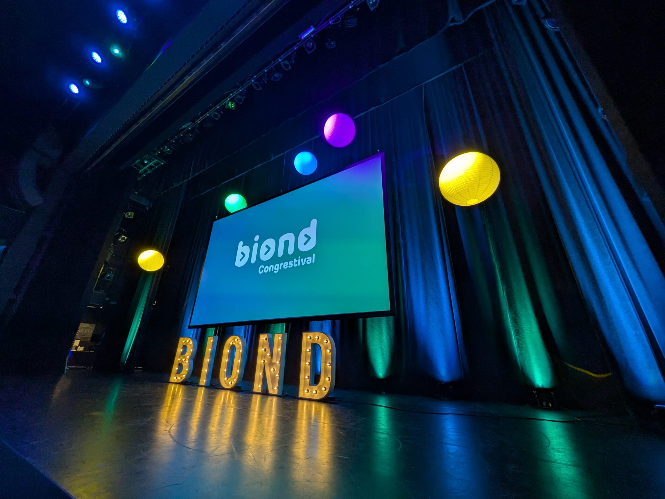Een theaterzaal met een presentatiescherm waarop staat "BiOND Congrestival"